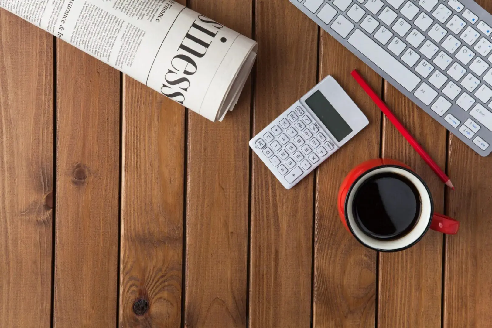 A cup of coffee, calculator and keyboard on a table.