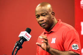 A man in red shirt talking into microphone.