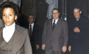 A man in suit and tie standing next to a statue.