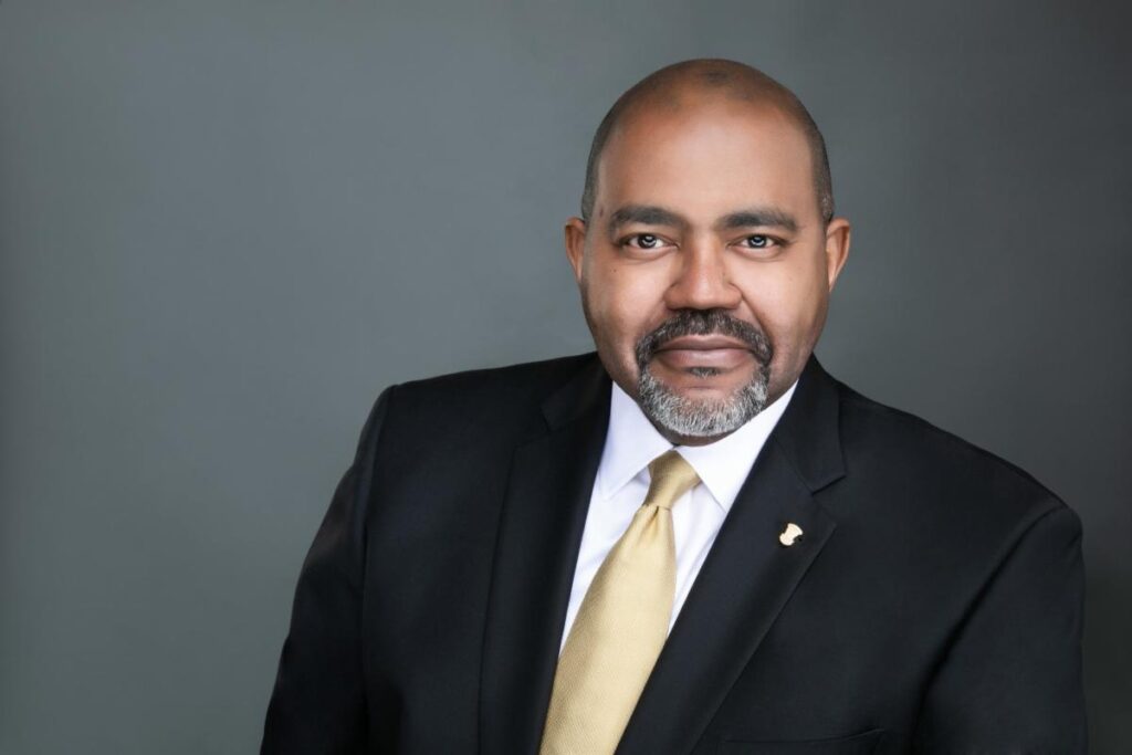 A man in a suit and tie standing up against a gray background.