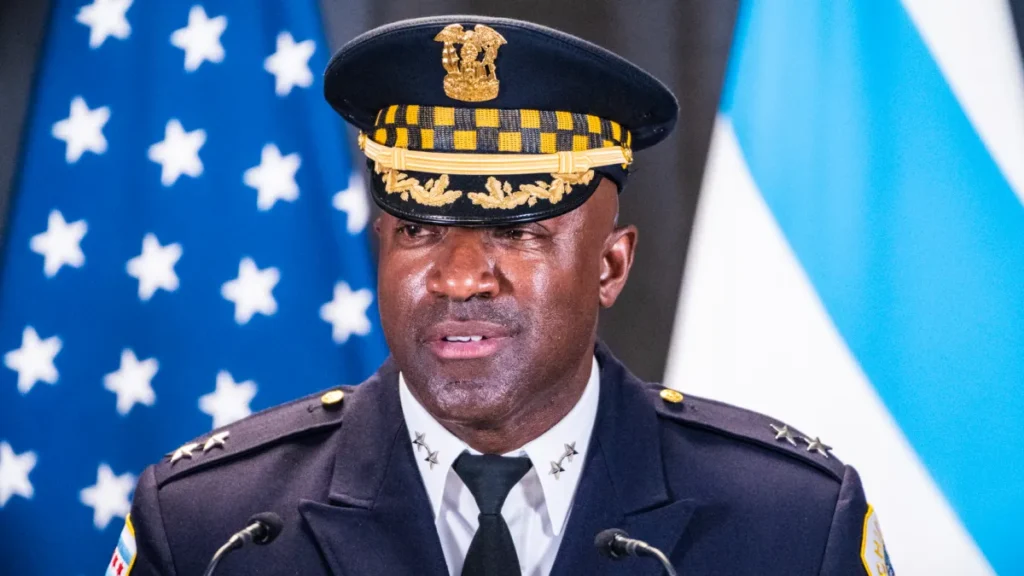 A man in uniform is standing next to two flags.