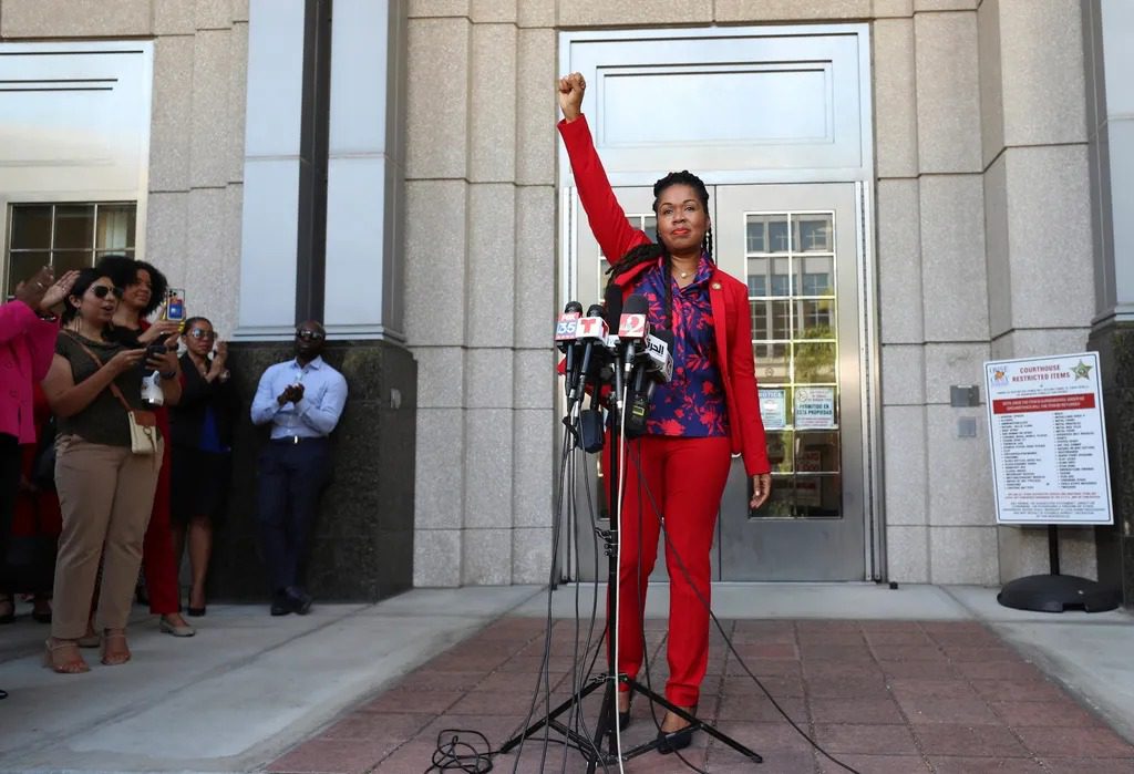 A person in red pants and a jacket holding up a fist.