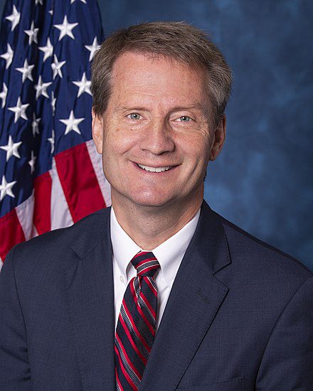 A man in a suit and tie next to an american flag.