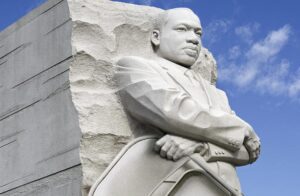 A statue of martin luther king jr. Is shown in front of the washington monument.