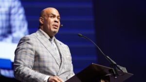 A bald man in a suit is speaking at a podium.