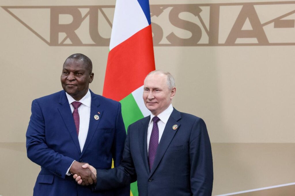 Two men shaking hands in front of a russian flag.