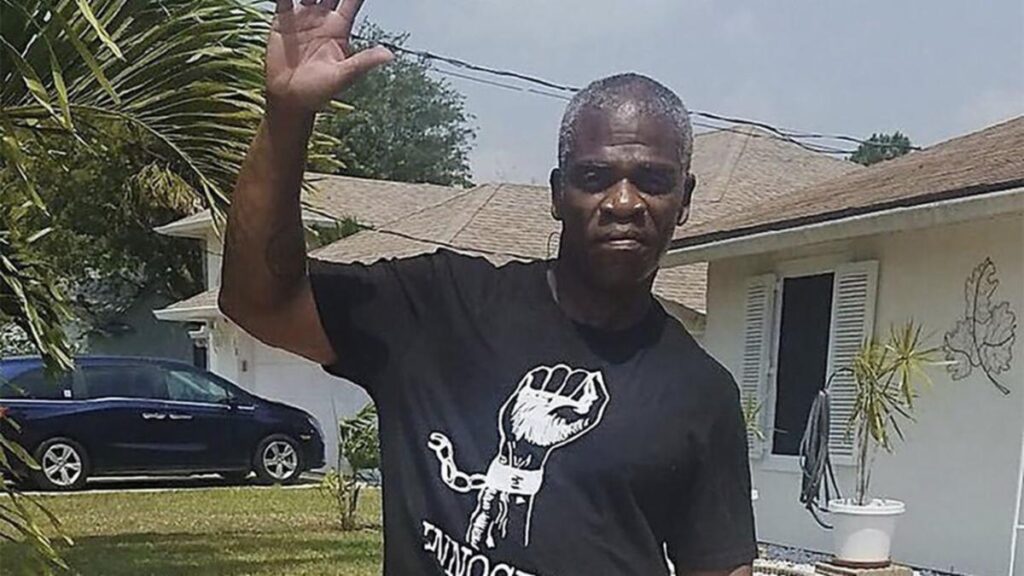 A man in black shirt waving at the camera.