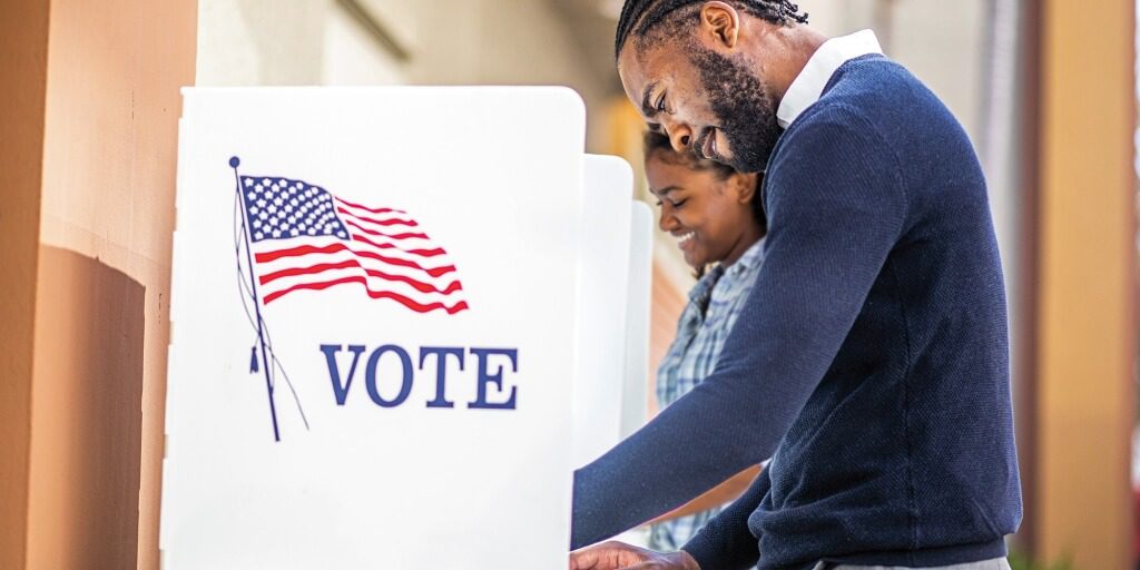 Two people standing in front of a voting booth.