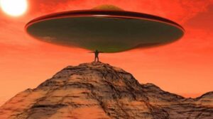 A man standing on top of a mountain under an alien flying saucer.