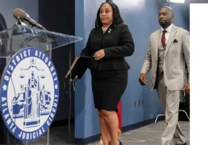 A woman in black suit and red tie walking next to a podium.