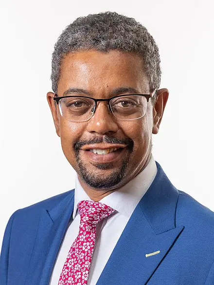 Man in blue suit with pink tie and glasses.