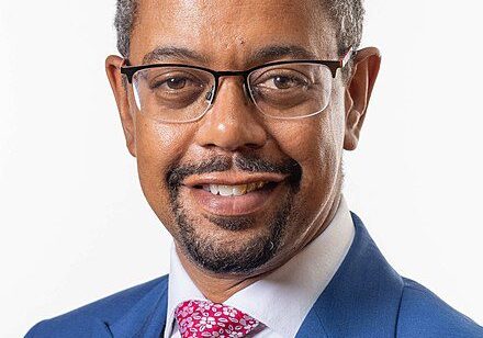 Man in blue suit with pink tie and glasses.