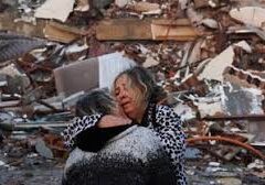 Two women hug in front of a pile of rubble.